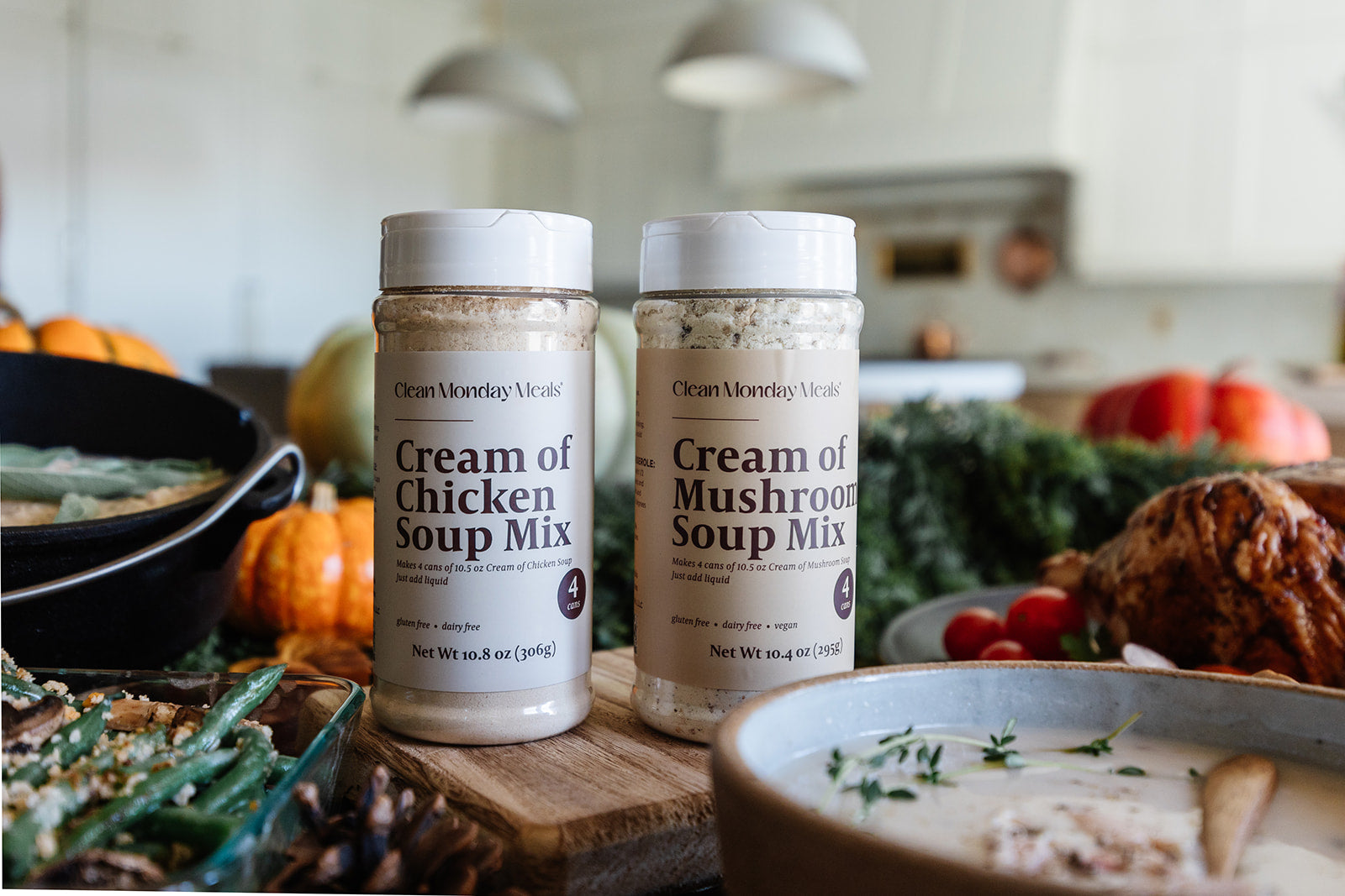 Two jars of Clean Monday Kitchen soup mix on a kitchen counter with pumpkins and a bowl of soup.