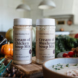 Two jars of Clean Monday Kitchen soup mix on a kitchen counter with pumpkins and a bowl of soup.