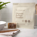 Clean Monday Meals Organic Ramen Noodles package with noodles and seasoning on a kitchen counter.