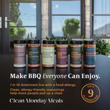 Six jars of barbecue seasonings lined up on a dark countertop in front of a window. The products include Everyday Beef Seasoning, Billionaire BBQ Seasoning, Zest & Herb Chicken Seasoning, Bold Bee BBQ Seasoning, Grit & grind BBQ Seasoning, and Bayou Salt Seasoning.