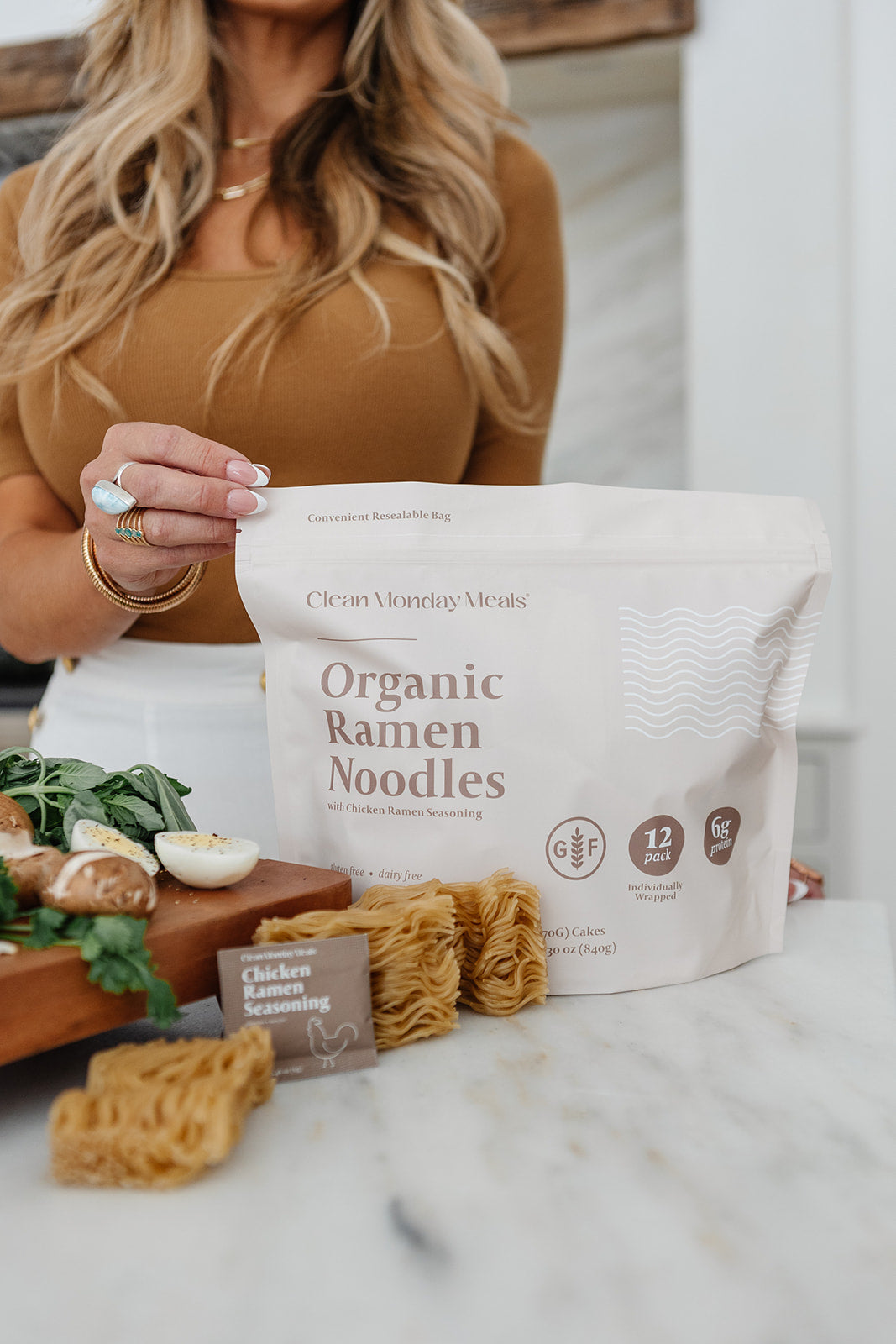 Person holding a bag of Organic Ramen Noodles with ingredients on a marble surface