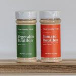 Two bouillon containers, one green and one red, on a wooden surface with a white background.