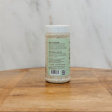 A bottle of cream of celery soup mix with a white cap and light green label, standing on a wooden surface against a marble background.