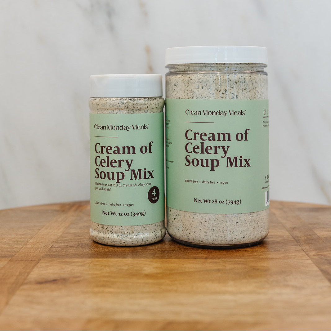 Two jars of Clean Monday Meals Cream of Celery Soup Mix on a wooden cutting board against a marble background.