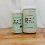 Two jars of Clean Monday Meals Cream of Celery Soup Mix on a wooden cutting board against a marble background.