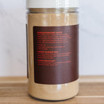 A clear plastic jar of Worcestershire Sauce with a white lid and a dark brown label, sitting on a wooden surface against a light marble background.