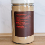 A clear plastic jar of Worcestershire Sauce with a white lid and a dark brown label, sitting on a wooden surface against a light marble background.