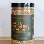 Jar of Grit & Grind BBQ Seasoning on a wooden surface with a white background