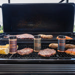 Grill with various meats and seasoning bottles on a sunny day