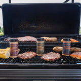 Grill with various meats and seasoning bottles on a sunny day