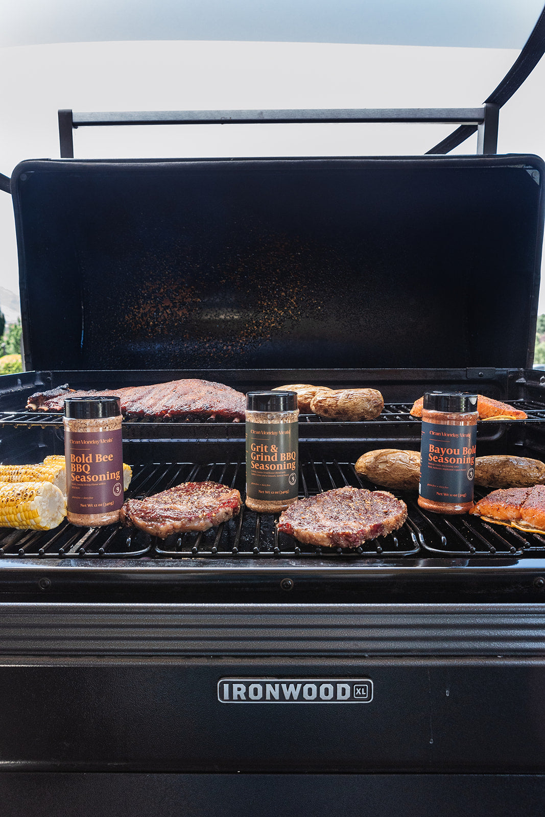 Grill with various meats and seasoning bottles on a sunny day