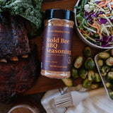 Bottle of Bold Bee BBQ seasoning on a wooden board with vegetables and salad.