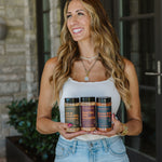 Woman holding three bottles of a product in front of a stone building.
