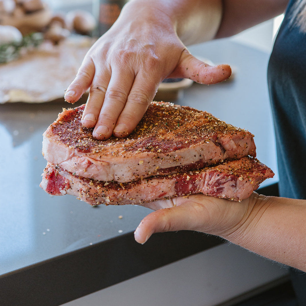 Person holding a seasoned steak on a kitchen counter