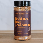 Bottle of Bold Bee BBQ Seasoning on a wooden surface with a white background