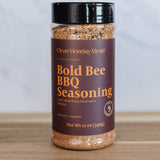 Bottle of Bold Bee BBQ Seasoning on a wooden surface with a white background