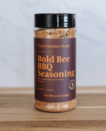 Bottle of Bold Bee BBQ Seasoning on a wooden surface with a white background
