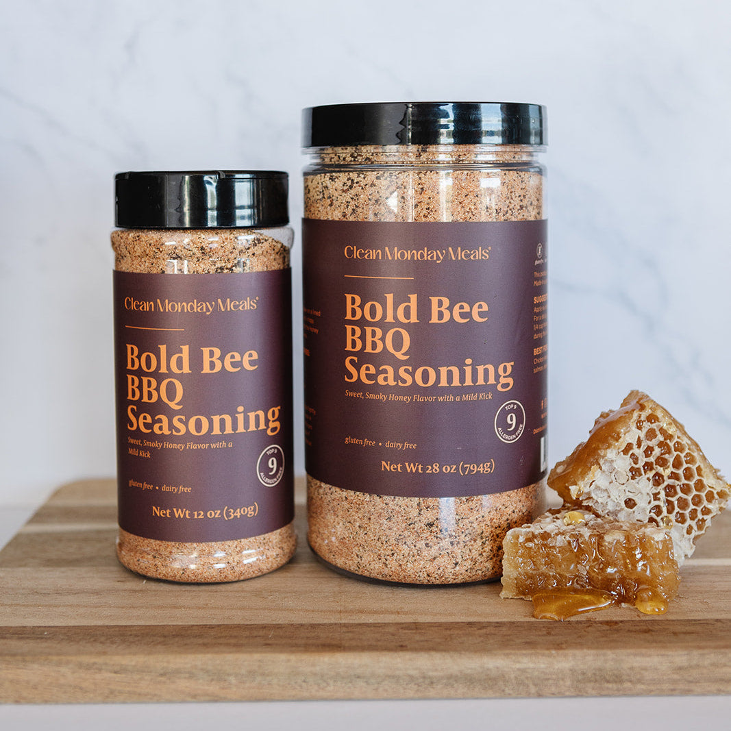 Two jars of Bold Bee BBQ Seasoning on a wooden surface with honeycomb and honey.