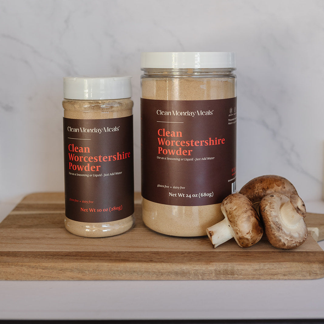 Two jars of Cran Morning Meals Clean Worcestershire Powder on a wooden cutting board with mushrooms, set against a white marble backsplash.