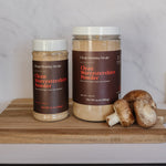 Two jars of Cran Morning Meals Clean Worcestershire Powder on a wooden cutting board with mushrooms, set against a white marble backsplash.