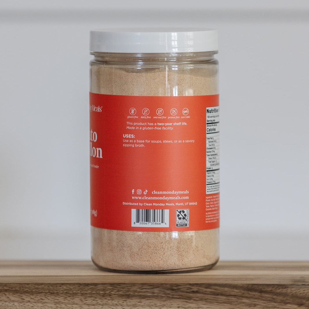 Jar of Clean Monday Meals tomato bouillon on a wooden surface, white background. 