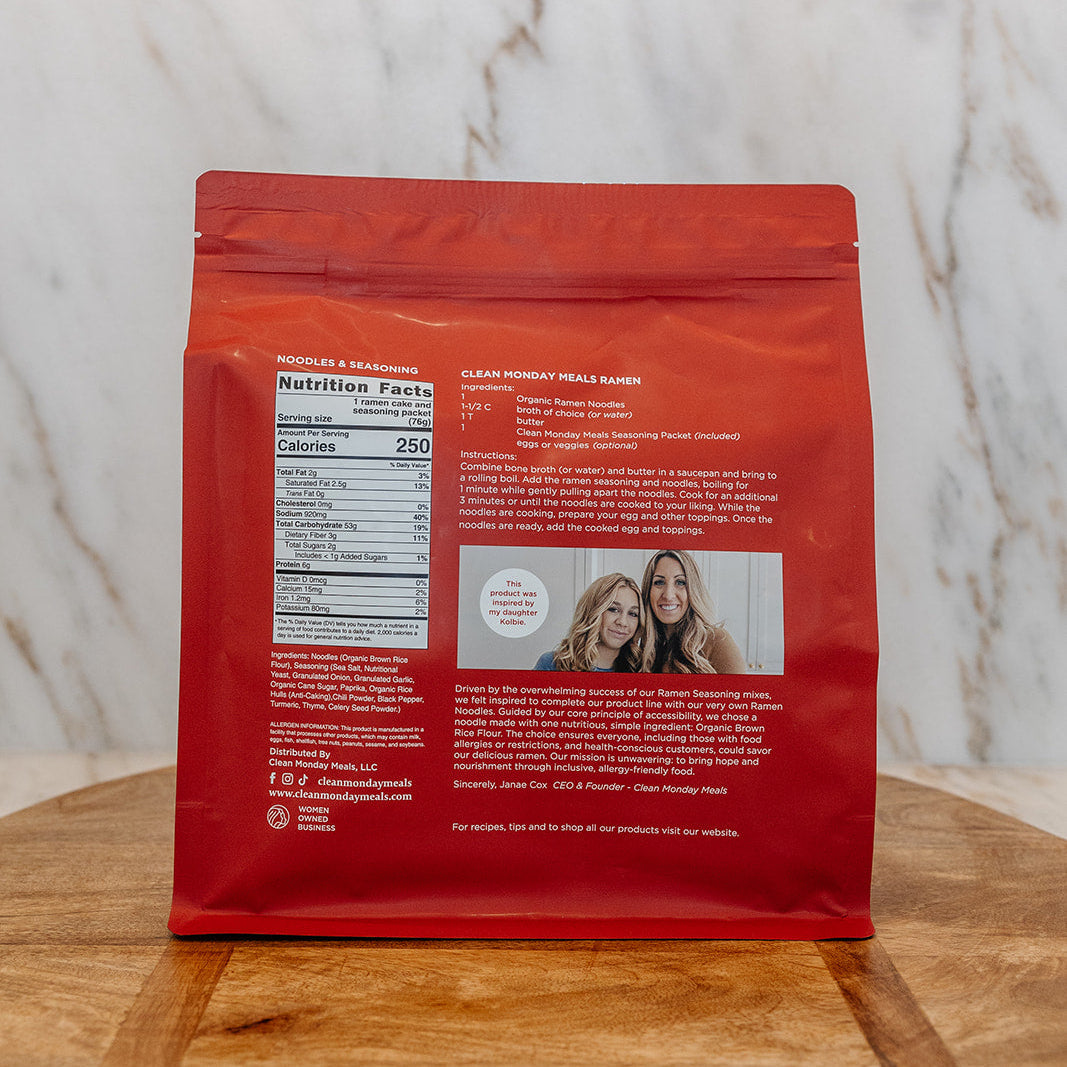 A red stand-up pouch of coffee beans, showing the back label with nutrition facts, product details, and a small photo of two women, placed on a wooden surface against a marble-patterned background.