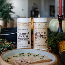 Two containers of Cream of Chicken and Mushroom Soup Mix on a table with a festive background.