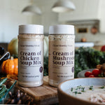 Two jars of Clean Monday Kitchen soup mix on a kitchen counter with pumpkins and a bowl of soup.