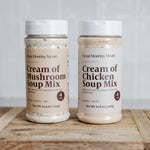 Two jars of Clean Monday Meals soup mix on a wooden surface with a neutral background.