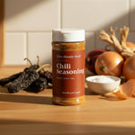 Jar of chili seasoning on a counter top with other herbs around it. 