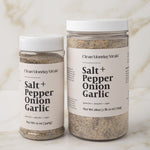 Two containers of 'Salt + Pepper Onion Garlic' seasoning on a marble surface.