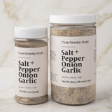 Two containers of 'Salt + Pepper Onion Garlic' seasoning on a marble surface.