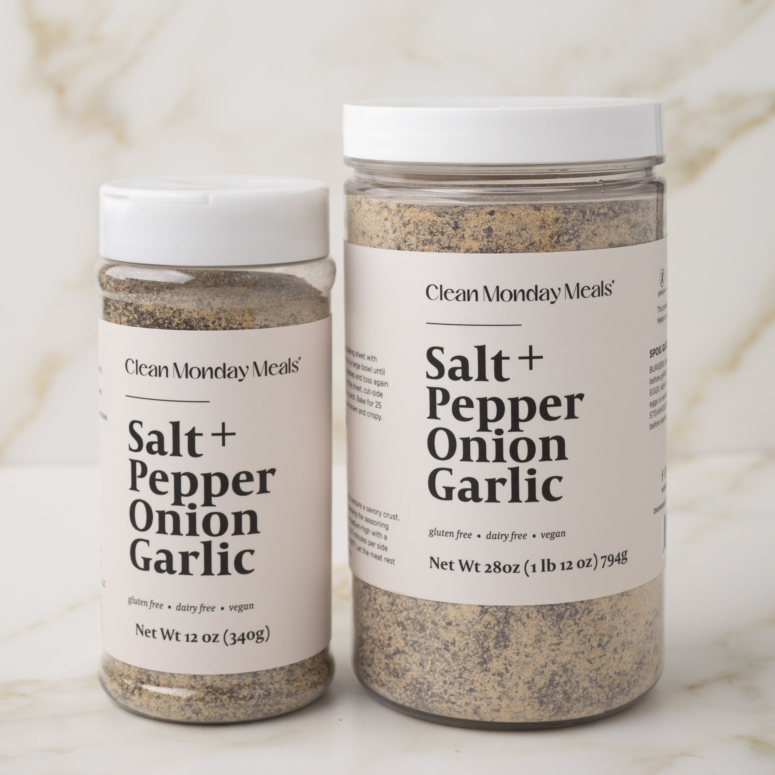 Two containers of 'Salt + Pepper Onion Garlic' seasoning on a marble surface.