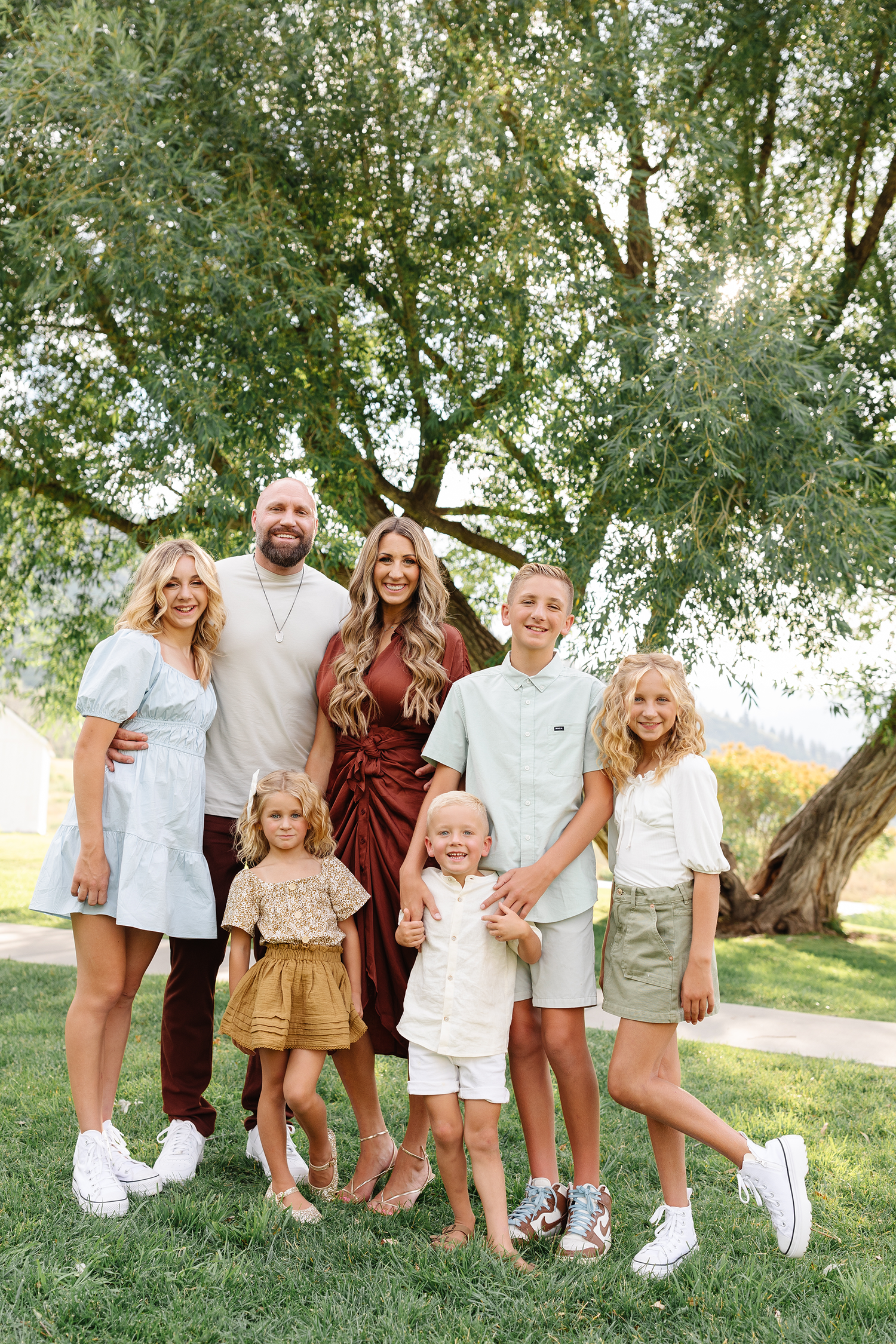 Kevin and Janae Cox with their five children standing under a tree while taking family pictures.