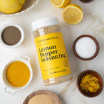 Lemon pepper seasoning container with lemons and spices on a marble surface
