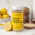 Bottle of Lemon Pepper Seasoning with lemons and a wooden pepper grinder on a kitchen counter.