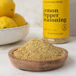 Wooden bowl of lemon pepper seasoning with a bottle of the product in the background.