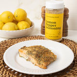 Salmon fillet on a plate with lemon pepper seasoning and lemons in the background.