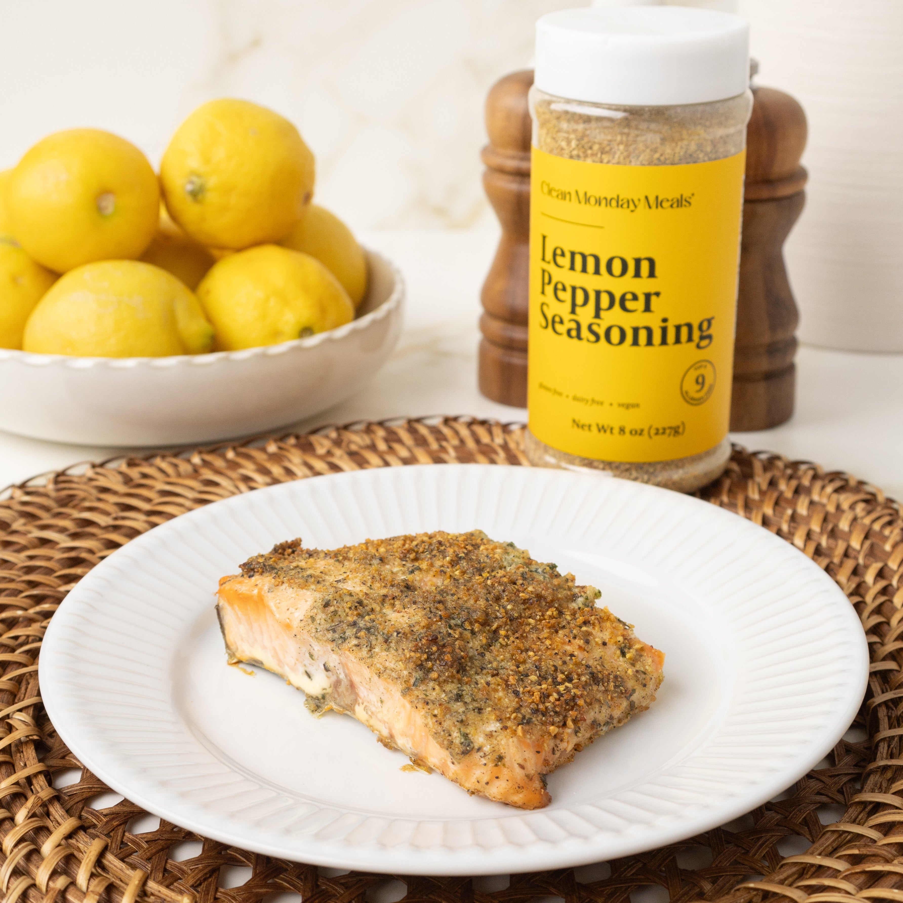 Salmon fillet on a plate with lemon pepper seasoning and lemons in the background.