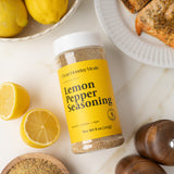 Jar of Lemon Pepper Seasoning with lemons and a pepper grinder on a light surface