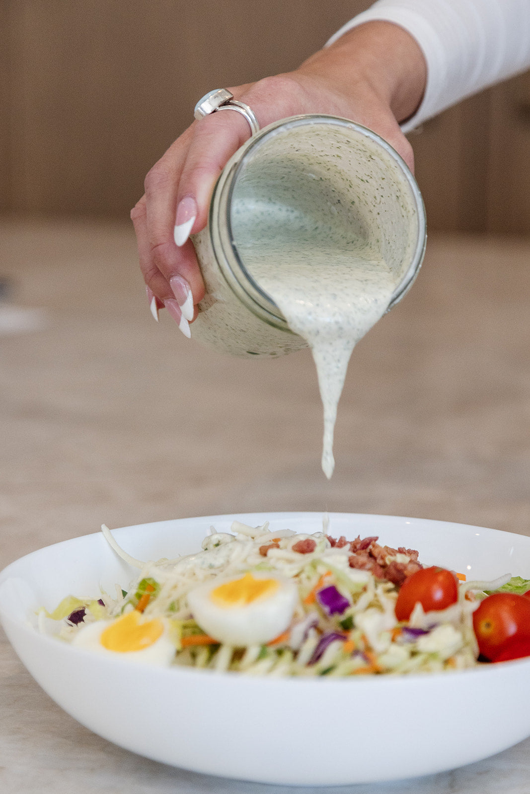 Pouring a mason jar of Clean Monday Meals Ranch Seasoning on a salad. 